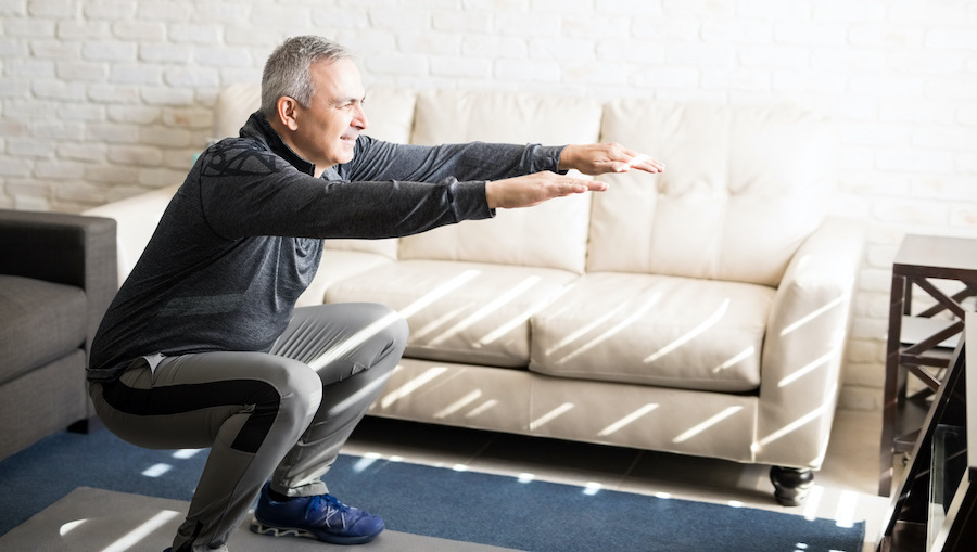 Mature man doing squats workout at home